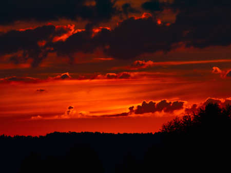 Beautiful red sunset over the forest. Dramatic sky with clouds.