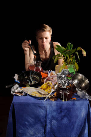 A young man with a spoon sits behind dirty tableの写真素材