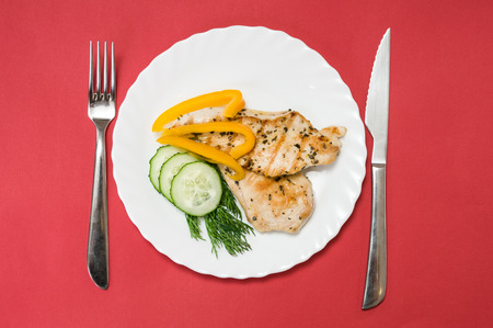 grilled chicken fillet on a white plate and red backgroundの写真素材