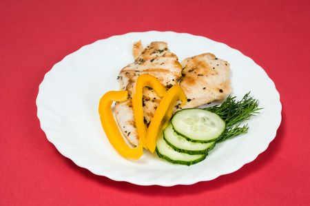 grilled chicken fillet on a white plate and red backgroundの写真素材