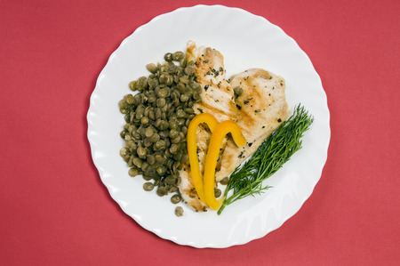 grilled chicken fillet with lentils on a white plate and red backgroundの写真素材