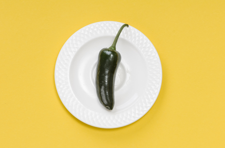 Single green jalapeno pepper on white plate on yellow backgroundの写真素材