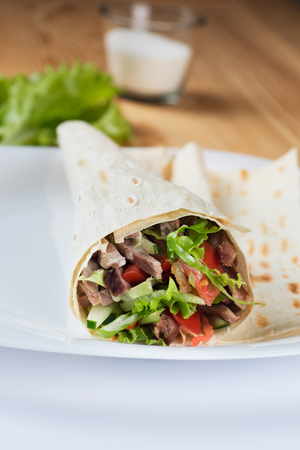 Tortilla with a delicious grilled pork meat on white plate and fresh mixed leafy green salad tomato amd cucumber filling.の写真素材