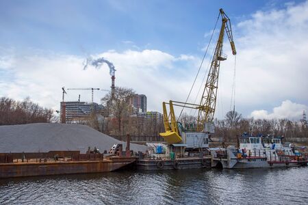 Old river barge with a crane on the background of unfinished buildings. Moscow river.の写真素材