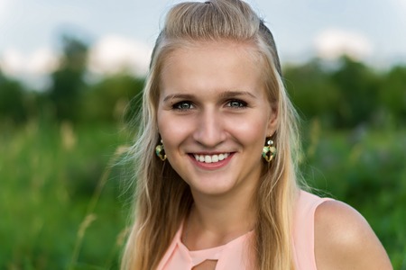 Closeup portrait of a happy young blond woman smiling in a summer park.の写真素材