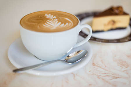 Cappuchino or latte coffe in a white cup on with a cake on a light beige table.の写真素材