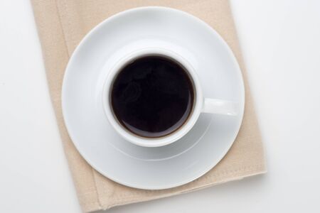 Black coffee with bubbles in white cup on towel with coffee beans, view from above.の写真素材