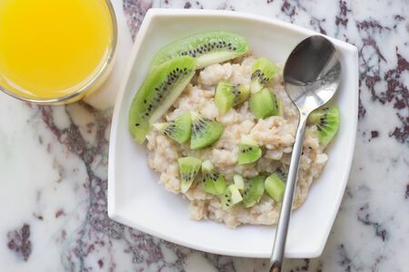Bowl of oatmeal porridge with kiwi on marble table, with orange juice, hot and healthy breakfast every day, diet foodの写真素材