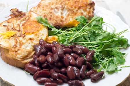 A delicious home style breakfast. Omelette with backed beans on a white plate with arugula salad.