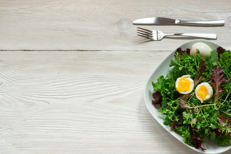Fresh mixed green salad on white plate on wooden table close up