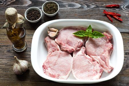 Raw Pork Loin Steaks in a dish on wooden table. Ready for roasting.の写真素材