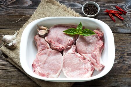 Raw Pork Loin Steaks in a dish on wooden table. Ready for roasting.の写真素材