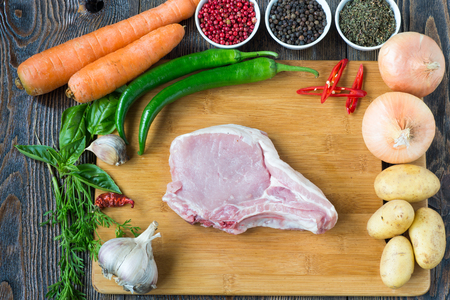 Raw Pork Loin Steaks on cutting board with basil, rose and red pepper, potato, onion, garlic, cilantro ready for cooking. Rustic style.の写真素材