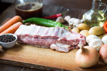 Raw uncooked Pork ribs  on wooden cut board ready to cook with vegetables, served over black textured background.の写真素材