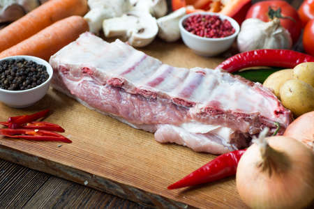 Raw uncooked Pork ribs  on wooden cut board ready to cook with vegetables, served over black textured background.の写真素材
