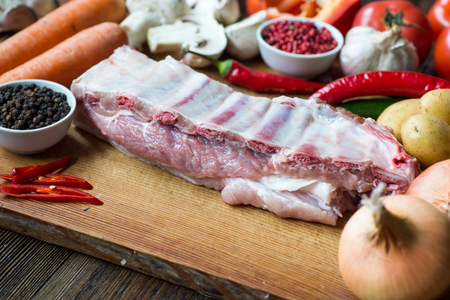 Raw uncooked Pork ribs  on wooden cut board ready to cook with vegetables, served over black textured background.の写真素材