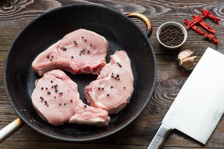 Raw Pork Loin Steaks in a dish on wooden table. Ready for fryの写真素材
