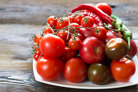Tomatoes of different kinds on a wooden  table in a plate side view. Table still life, food.の写真素材