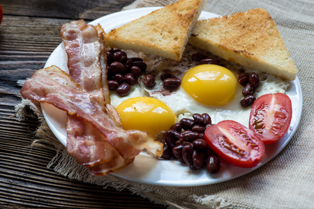 English breakfast with bacon, sausage, fried egg, baked beans on white plateの写真素材