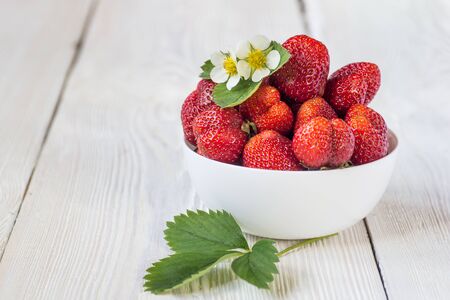 Fresh strawberries in a white porcelain bowl on wooden table in rustic style, selective focusの写真素材