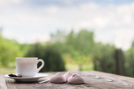 Delicate, delicious marshmallow and a cup of tea on a wooden table, summer garden backgroundの写真素材