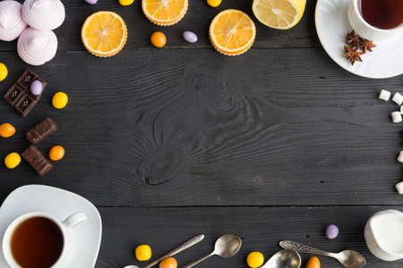 An assortment of  tea, coffee, marshmallow and chocolate, orange, pink zephyr and colorful dragee on black wooden backgroundの写真素材