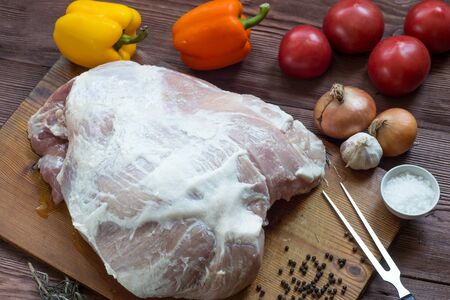 Raw pork leg on wooden cutting board ready for cooking with vegetablesの写真素材