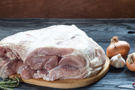Raw pork leg on wooden cutting board ready for cooking with vegetablesの写真素材