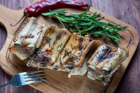 Delicious barbecued ribs  served with fresh herbs on an rustic wooden chopping board in a country kitchenの写真素材
