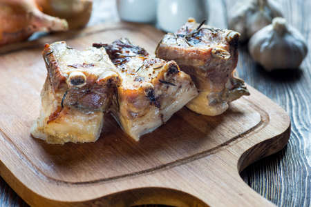 Delicious barbecued ribs served with fresh herbs on an rustic wooden chopping board in a country kitchenの写真素材