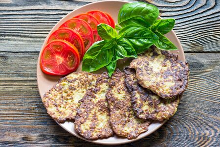 Zucchini pancakes on a plate with basil and tomato on rustic wooden table.の写真素材