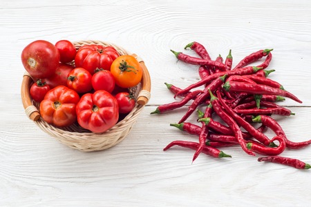 Fresh red tomatoes in a basket and chilli pepper on a white wooden backgroundの写真素材