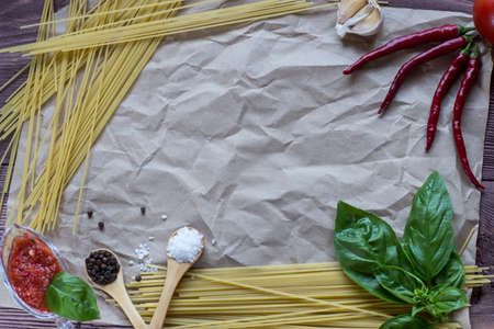 Italian spaghetti on a wooden table with bunch tomatoes, rosemary, garlic and cup of oil. Top view.の写真素材