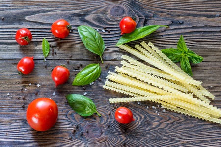 Tomatoes with basil and pasta  in colander on wooden table background. Food composition. Top viewの写真素材