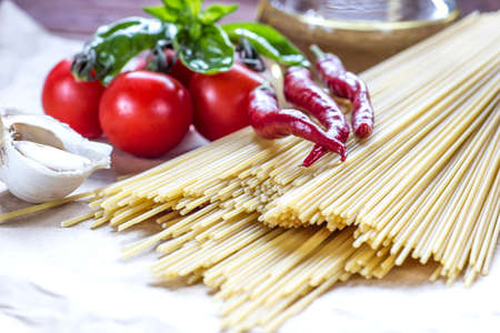 Italian spaghetti on a wooden table with bunch tomatoes, rosemary, garlic and cup of oil. Top view.の写真素材