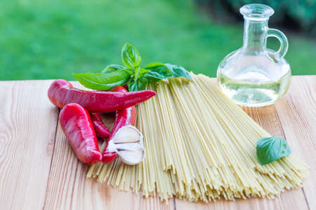Italian spaghetti on a wooden table with bunch tomatoes, rosemary, garlic and cup of oil. Top view. Summer garden backgroundの写真素材