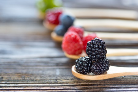 Berries in wooden spoons on wooden background. Raspberries, Blueberries, Blackberry, currant, gooseberrys.  Health, Diet, Gardening, Harvest Conceptの写真素材