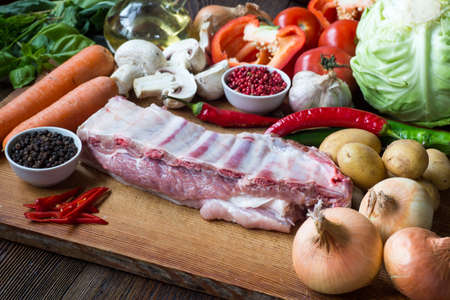 Raw uncooked Pork ribs  on wooden cut board ready to cook with vegetables, served over black textured background.の写真素材
