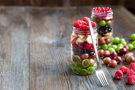 Mason jar filled with gooseberries, black and red currant, peach and raspberry  fresh fruit on rustic wooden background.の写真素材
