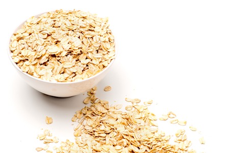 Food. Oatmeal on the table. Dry rolled oat flakes oatmeal in a white bowl on a white table.