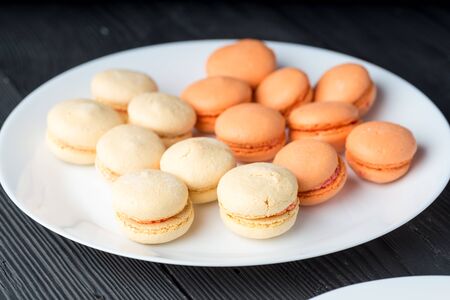 Fresh baked orange green macaroon pastry cookies (macarons, macaroni) on a white plate close up, low...