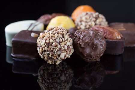 Delicious chocolates, rolled oats, pecan nuts, dates, coconut flakes on black background with...