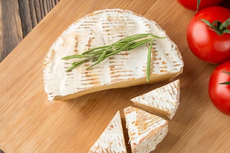 Cheese head of Brie cheese and rosemary and cherry tomato on wood cutting board, rustic style.の写真素材