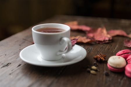Autumn composition. Cup of tea, macaroons, checkered plaid, dried leaves on white background. Autumn, cozy fall concept. Flat lay, top view, copy spaceの写真素材