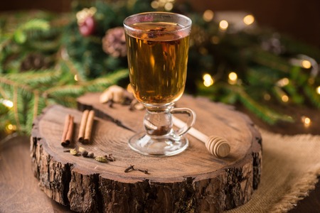 Christmas and Thanksgiving mulled apple cider with spices: cinnamon sticks, cloves, anise on white table with traditional rustic Christmas background flowers arrangement, Autumn and winter drink.の写真素材