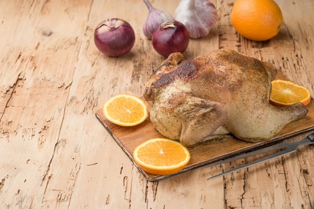Roasted chicken with orange served on wooden board on wooden table, top viewの写真素材