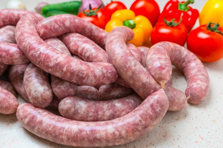 Raw sausage of beef and pork with spices and tomato, pepperm onion, cucumber, onionm garlic vegetables on white kitchen table.の写真素材