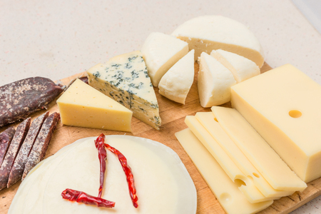 Various types of international soft , cheese, blue mold, gouda, feta and dried meat on wooden board.の写真素材