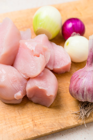 Sliced chicken breasts fillets with onion, pepper and rosmarin on wooden cutting board with knife on white wooden backgroundの写真素材