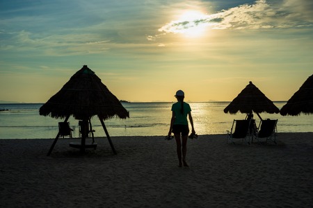 Silhouetted  walking woman and sun chairs with thatched umbrella on a beach at sunrise,の写真素材